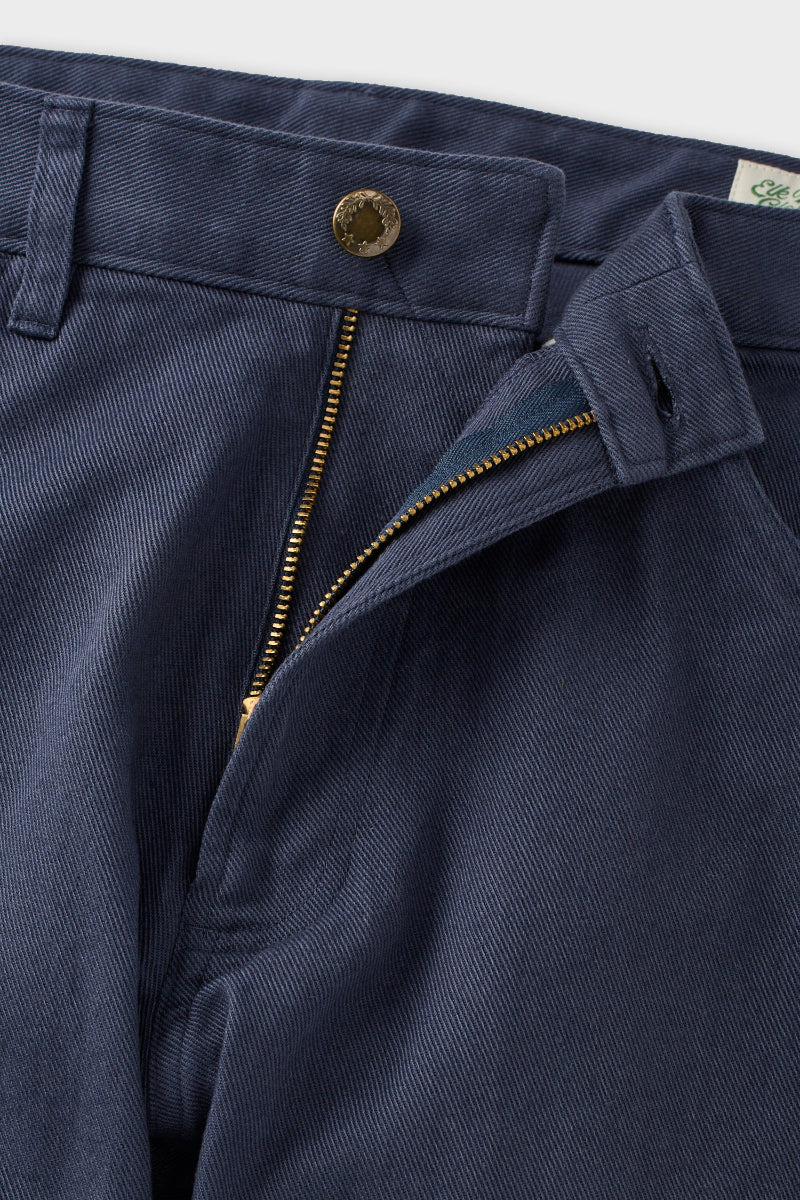 Close-up of navy blue trousers showing the waistband, a gold-tone button, a zippered fly opening, and part of the inner label.
