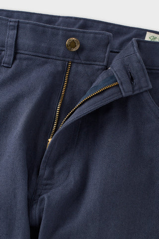 Close-up of navy blue trousers showing the waistband, a gold-tone button, a zippered fly opening, and part of the inner label.